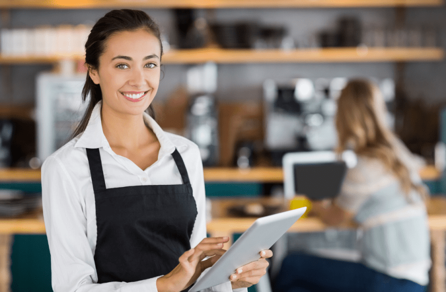 Retrato de uma empregada de mesa sorridente a utilizar um tablet digital num café